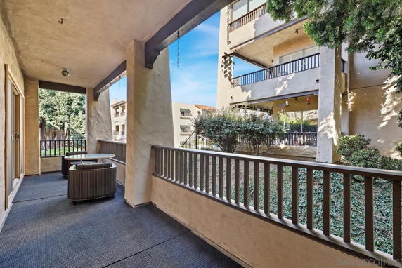 View from a covered balcony overlooking another apartment building and greenery.