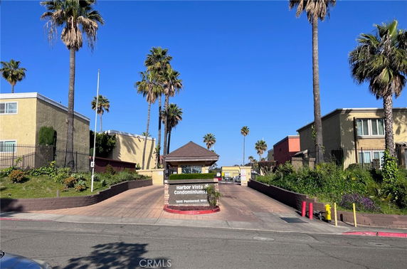 Front view of a gated condominium complex entrance with a sign and palm trees.