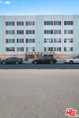 Front view of a multi-story apartment building with multiple windows and cars parked in front.