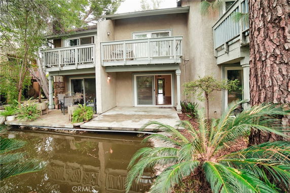 Front view of a two-story house with balconies and a patio near a water feature.