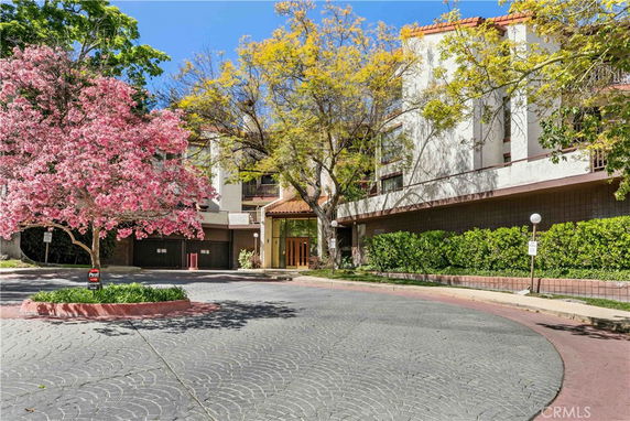 Front view of a multi-story building with a circular driveway and pink blossoming tree.