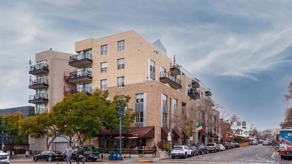Front view of a multi-story apartment building with balconies and ground-level storefronts.