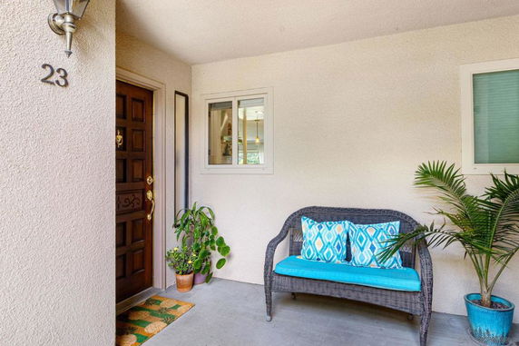 Front view of a house entryway with a brown door, a window, and a wicker bench.