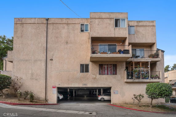 Front view of a multi-story apartment building with balconies and a parking area beneath.