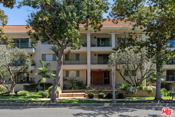 Front view of a multi-story building with balconies and large trees in front.
