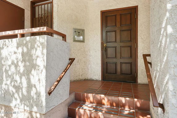 Front view of a house entrance with a wooden door and tiled steps.