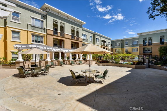 Perspective view of a multi-story apartment building with a courtyard featuring outdoor seating and umbrellas.