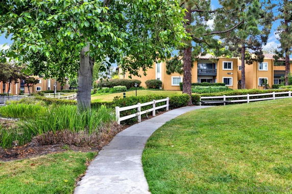 Pathway leading to a multi-story residential building surrounded by green lawns and trees.