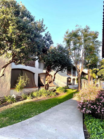 Front view of a two-story building with arches and a walkway surrounded by trees and plants.