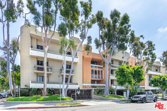 Front view of a multi-story residential building with balconies and surrounded by trees.