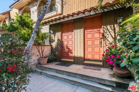 Front view of a house with two red doors and surrounding plants.