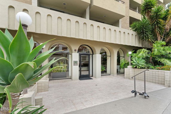 Front view of a building entrance with arched doorways and surrounding greenery.