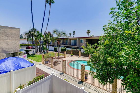 Outdoor swimming pool area with surrounding apartment buildings and palm trees.