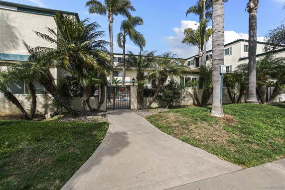 Front view of a multi-story building with palm trees along a walkway.