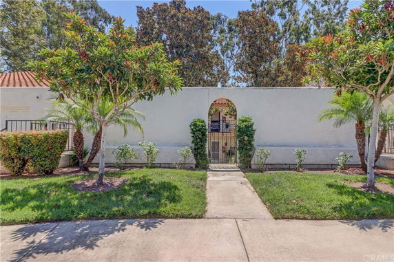 Exterior view of a gated entrance with a white wall and greenery around.