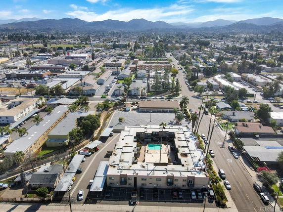 Aerial view of a residential area with multiple buildings and streets, with mountains in the distance and a central building with a swimming pool.