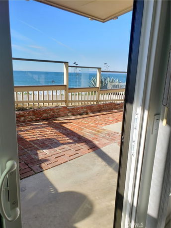 View of the ocean from an open doorway with a brick patio and glass railing.