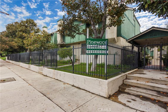 Front view of a multi-story residential building with a gated entrance and signboard.