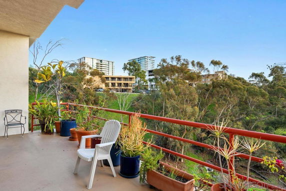 Balcony view with potted plants and distant multi-story buildings across a green landscape.