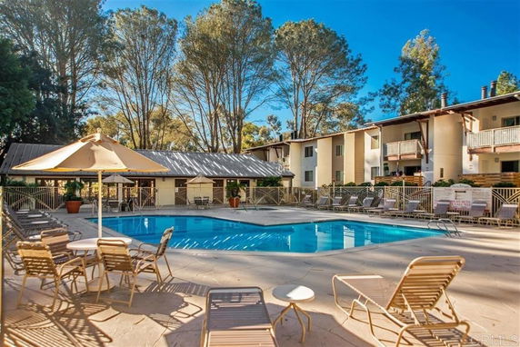Outdoor swimming pool area with surrounding lounge chairs and umbrella tables.