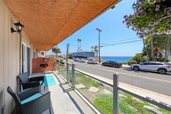 Outdoor view from a porch overlooking a street with cars and the ocean in the background.