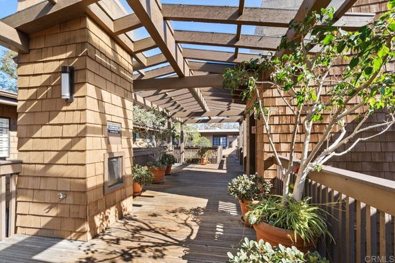 Wooden deck area with open trellis roof and potted plants on a rooftop.