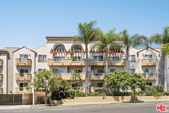 Front view of a multi-story apartment building with balconies and palm trees.