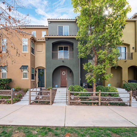 Front view of a three-story townhouse with balconies and entrance steps.