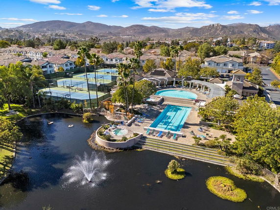 Aerial view of a residential area with tennis courts, a swimming pool, and a pond with a fountain.