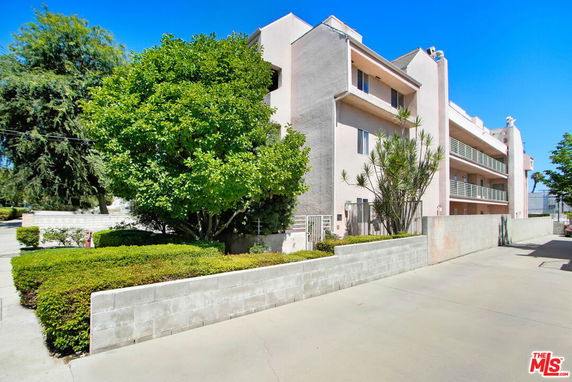 Front view of a multi-story residential building with balconies and surrounding greenery.
