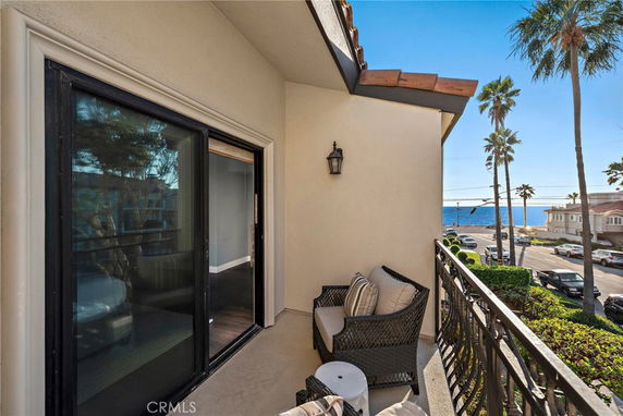 Balcony view overlooking a street with ocean and palm trees in the background.
