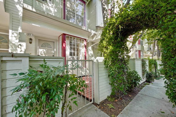 Front view of a multi-story house with a small gated entrance and lush greenery.