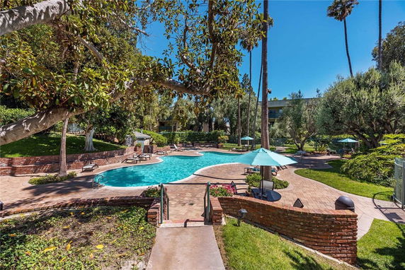 Outdoor swimming pool surrounded by trees and patio area with umbrellas.