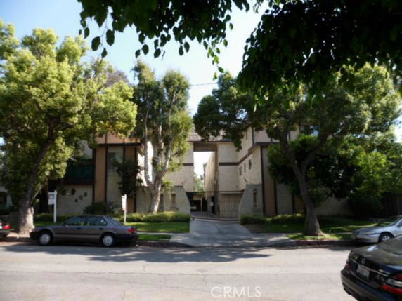 Front view of a multi-story residential building with a driveway and surrounding trees.