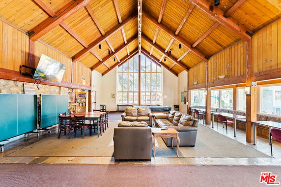Interior view of a clubhouse with high wooden ceilings, seating areas with couches, a dining table, and large windows.