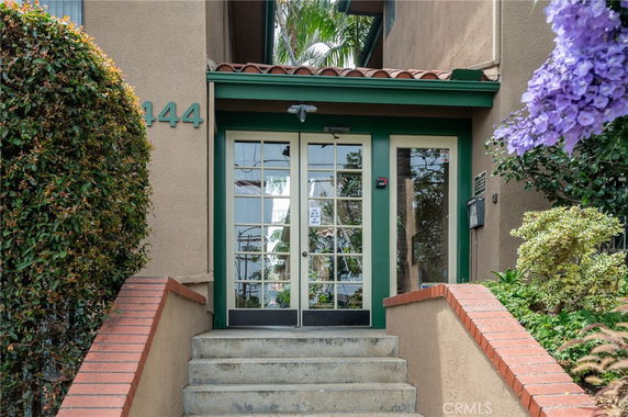 Front view of a building entrance with stairs and greenery.