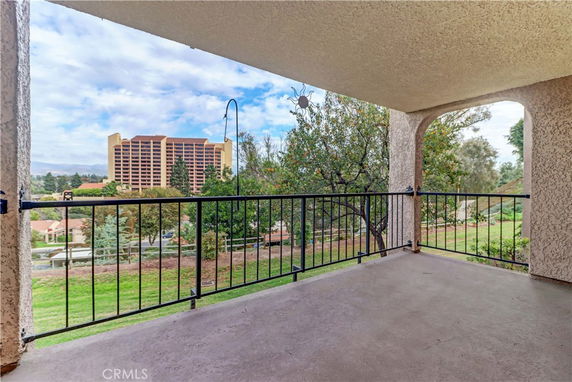 View from a covered balcony overlooking buildings and greenery.