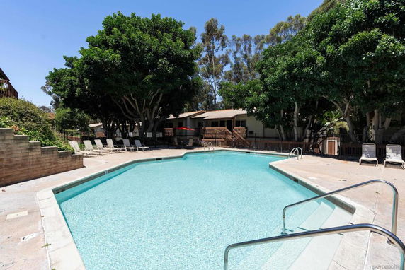 Outdoor swimming pool area with lounge chairs and surrounding trees.