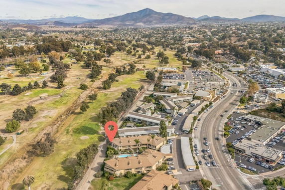 Aerial view of a residential area with adjacent golf course and distant mountains. A main road curves around the buildings.