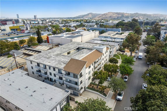 Aerial view of a multi-story apartment building with balconies, surrounded by other buildings and streets lined with trees.