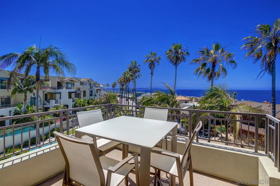 View from a balcony overlooking a coastal area with palm trees and nearby buildings.