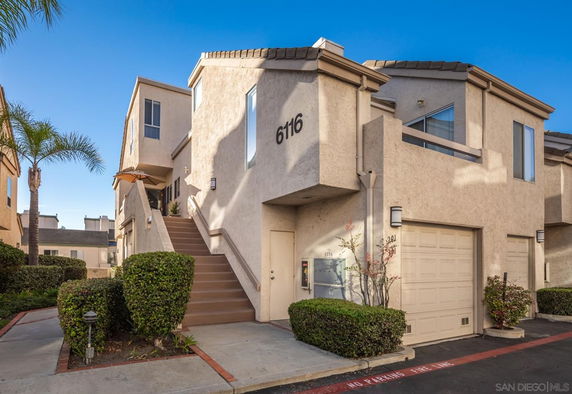 Front view of a modern two-story townhouse with a stairway leading to the entrance and a garage on the ground floor.