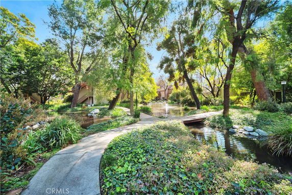 Pathway through a lush garden area with trees and a stream.