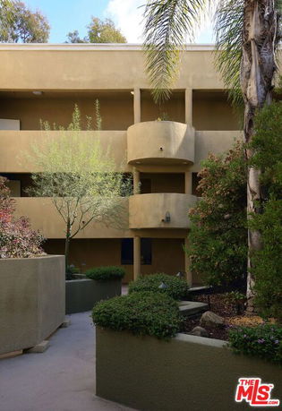 Front view of a two-story building with balconies and surrounding greenery.