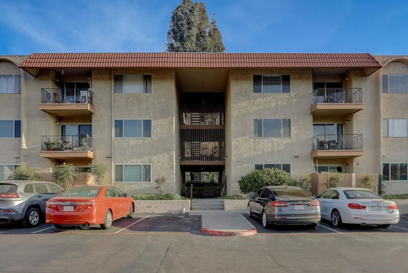 Front view of a multi-story apartment building with balconies and parking area.