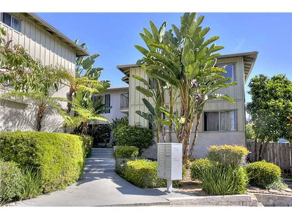 Front view of a multi-story residential building with plants and bushes.