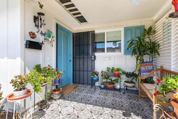Front porch of a house with decorative plants and a patterned tile floor.