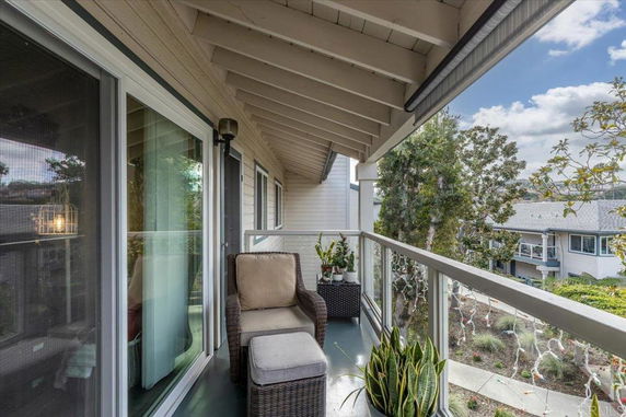 Balcony view with outdoor seating and distant buildings surrounded by trees.