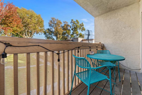 Outdoor balcony area with a blue table and chairs, overlooking trees.