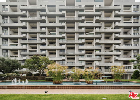 Front view of a multi-story building with balconies and a water feature in front.